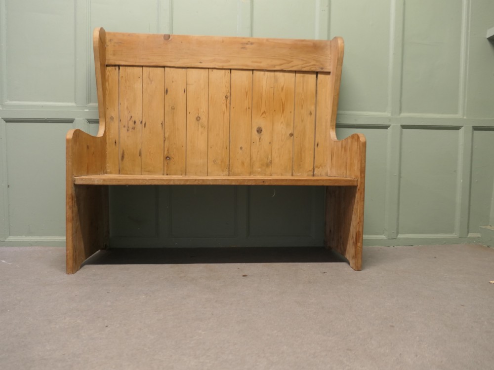 A high-back rustic pine settle bench featuring vertical planking and solid side armrests in a natural warm wood finish.