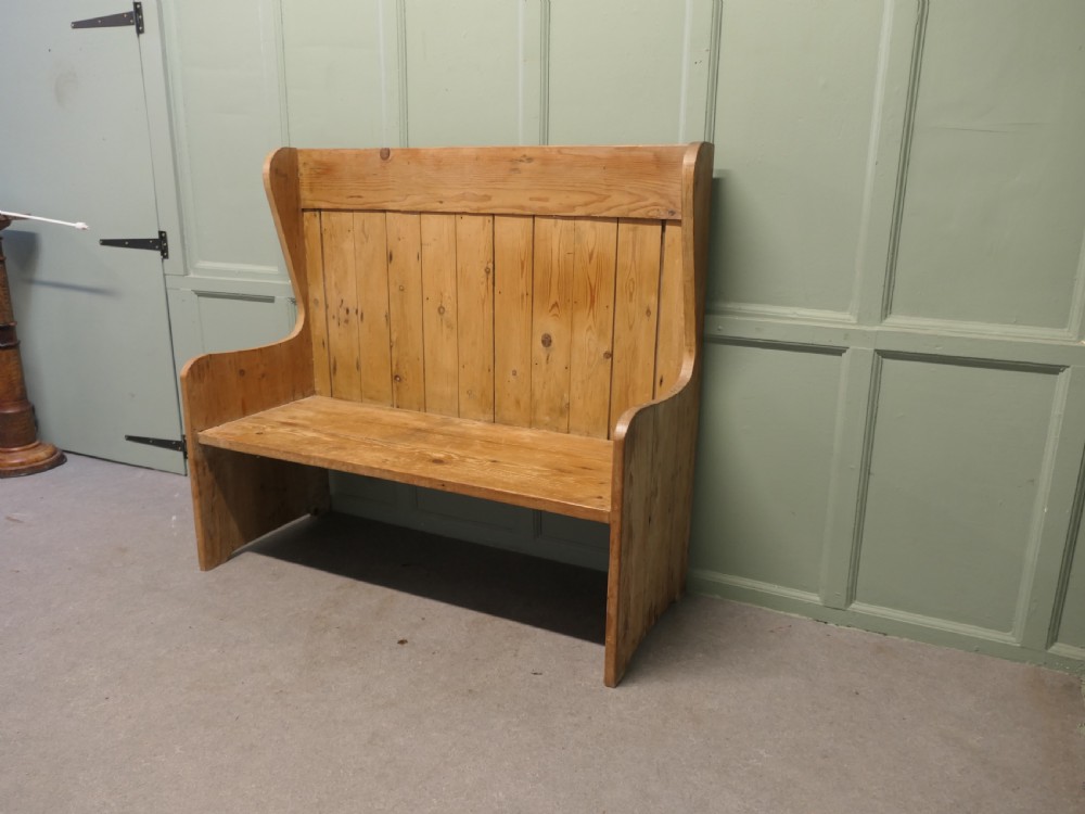 A high-back rustic pine settle bench featuring vertical planking and solid side armrests in a natural warm wood finish. View II
