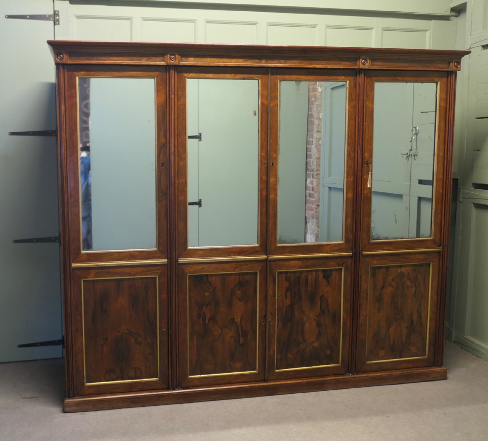 A nineteenth-century Regency rosewood four-door wardrobe with mirrored upper sections and brass stringing decoration.