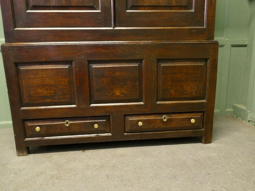 A tall dark Georgian oak housekeepers cupboard featuring two upper doors with arched fielded panels over a lower section with two drawers. View II
