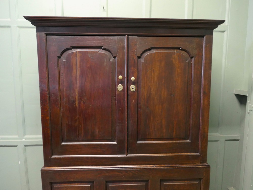A tall dark Georgian oak housekeepers cupboard featuring two upper doors with arched fielded panels over a lower section with two drawers. View III