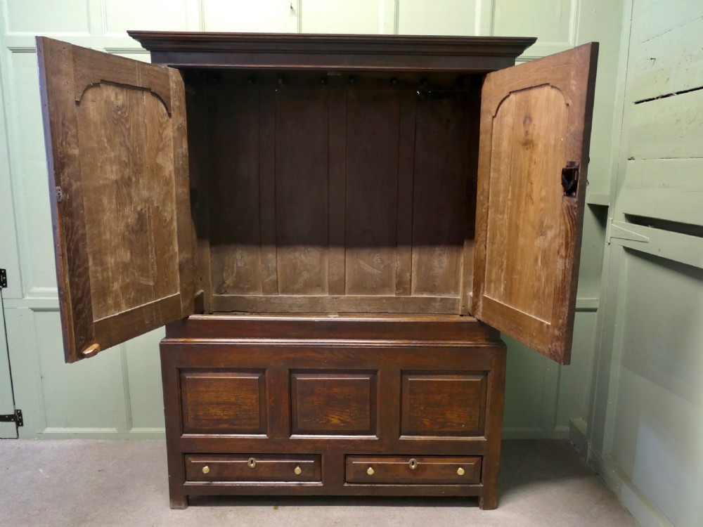 A tall dark Georgian oak housekeepers cupboard featuring two upper doors with arched fielded panels over a lower section with two drawers. View IV