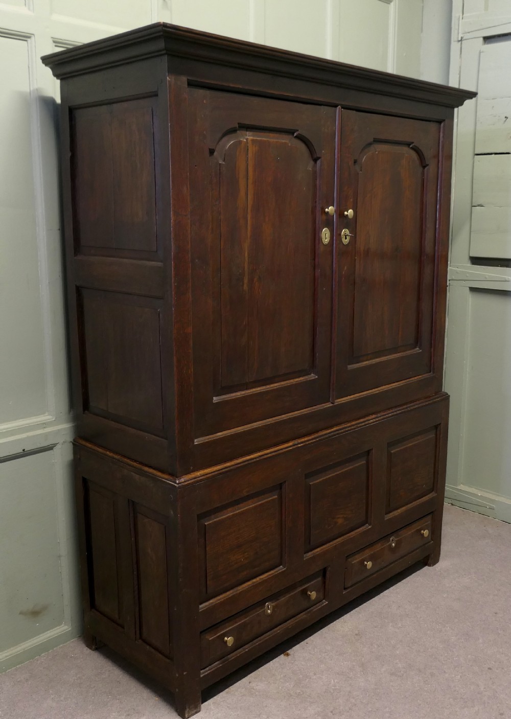A tall dark Georgian oak housekeepers cupboard featuring two upper doors with arched fielded panels over a lower section with two drawers. View VI