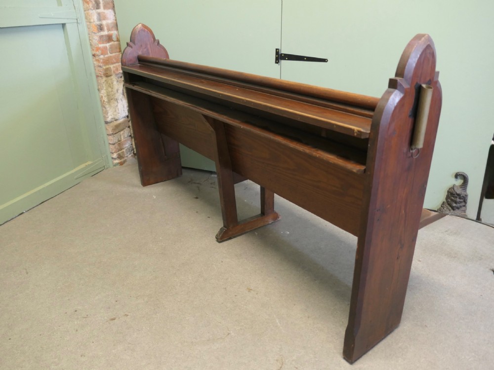 An antique Arts and Crafts pitch pine church pew featuring a solid panelled back and shaped bench ends. View II