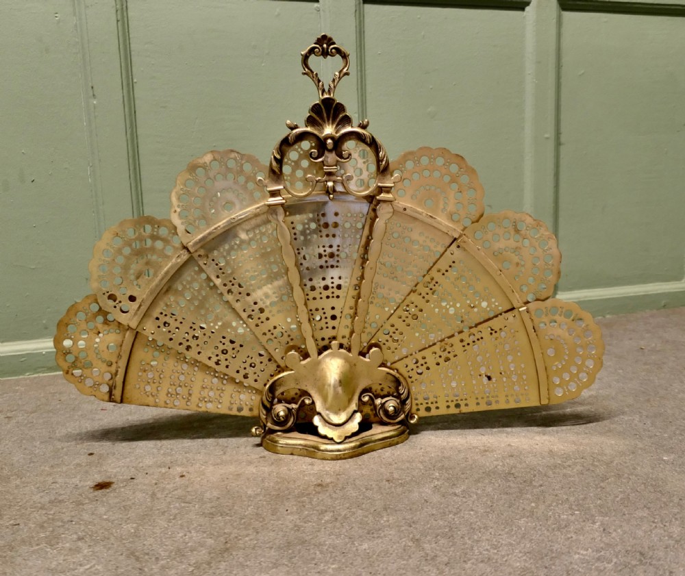 A French cast brass folding fire screen in the shape of a peacock tail with reticulated filigree blades and an ornate Rococo base.