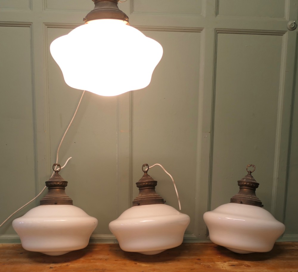 A set of four vintage industrial ceiling pendant lights featuring white opal glass shades and aged brass galleries.