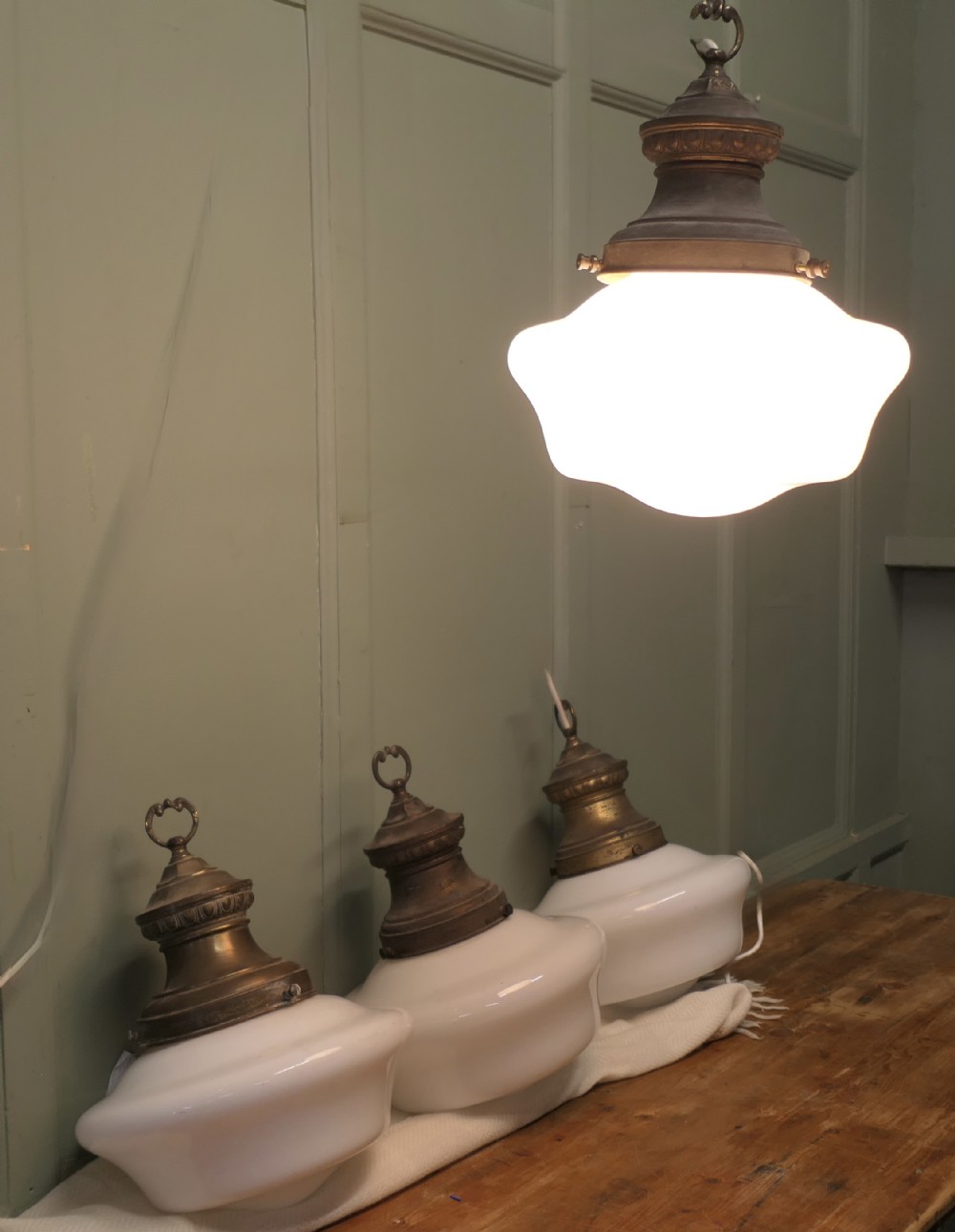 A set of four industrial ceiling lights with white opaline glass shades and patinated brass galleries featuring molded top collars and hanging rings.