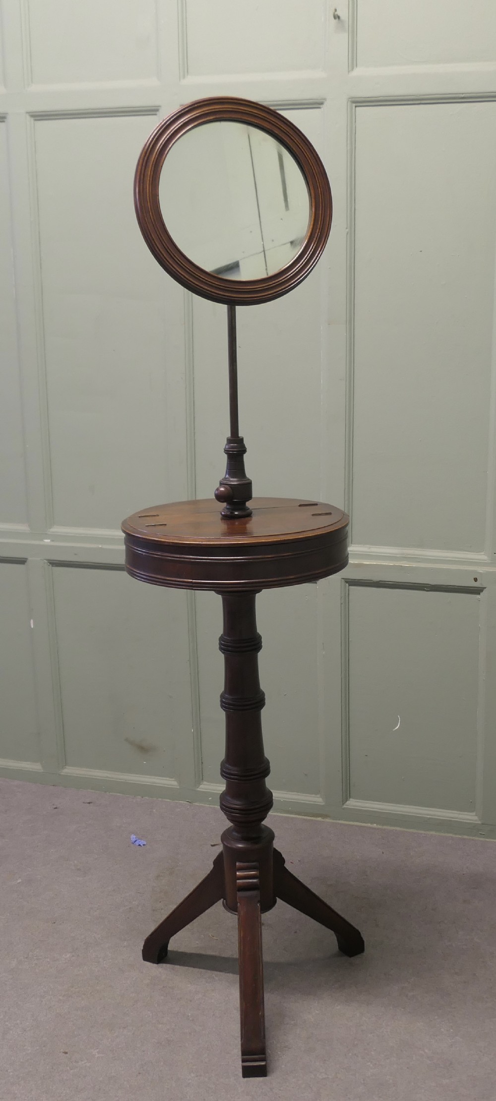 A Victorian dark mahogany freestanding shaving mirror featuring a circular frame, height-adjustable brass column, central round shelf, turned pedestal stem, and tripod legs.