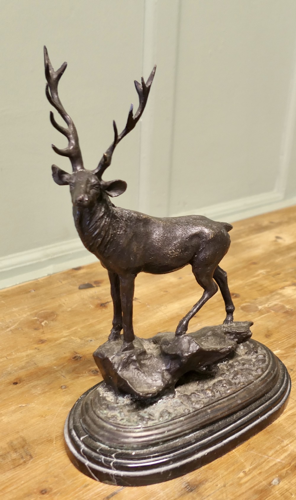 A dark bronze sculpture depicting a stag standing on a rock base mounted atop an oval black marble plinth.