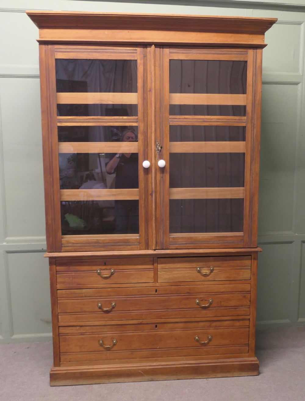 An Edwardian warm pine linen press with a glazed two-door upper cupboard revealing internal shelves above a base chest of four drawers.