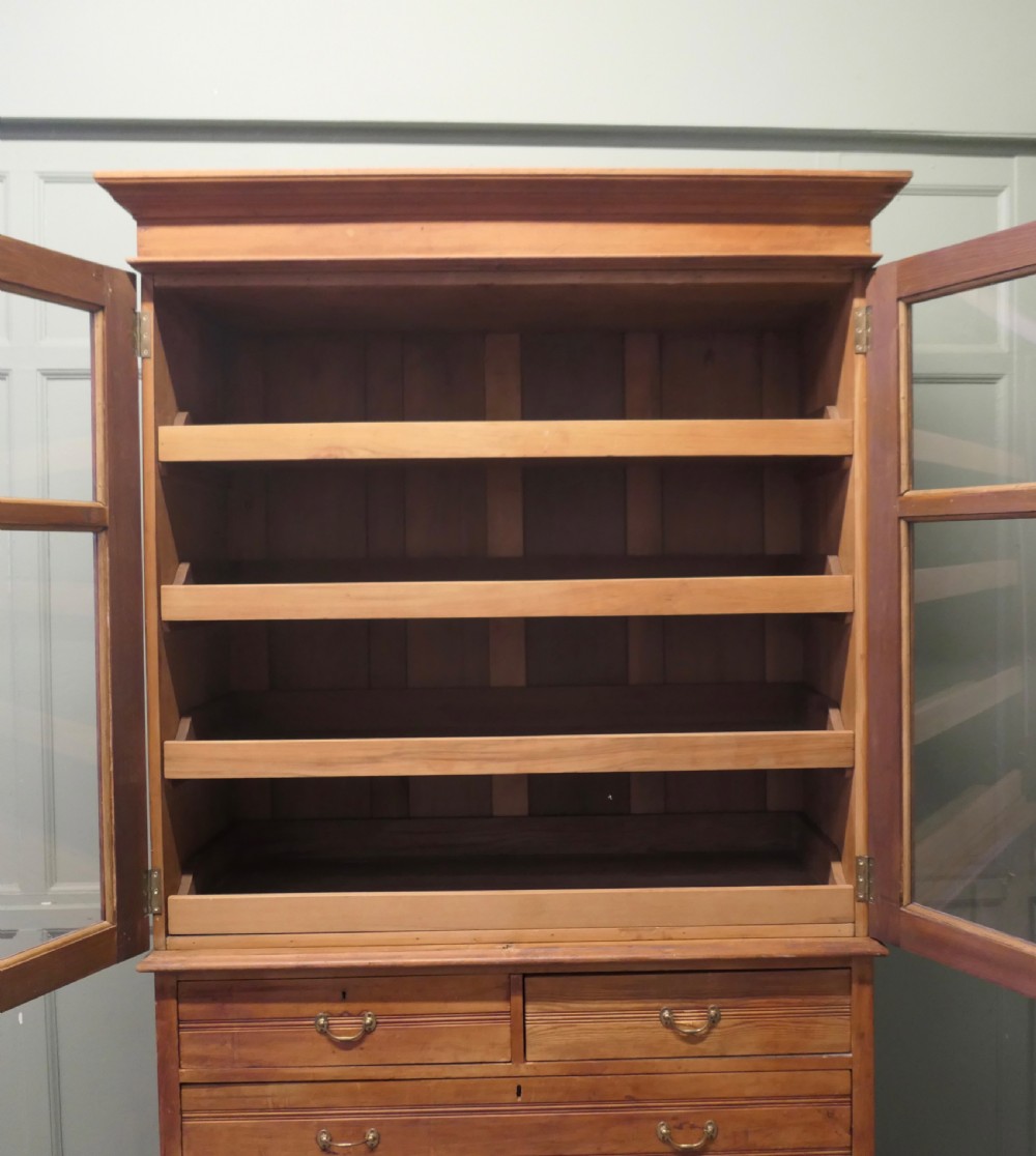 An Edwardian warm pine linen press with a glazed two-door upper cupboard revealing internal shelves above a base chest of four drawers. View II