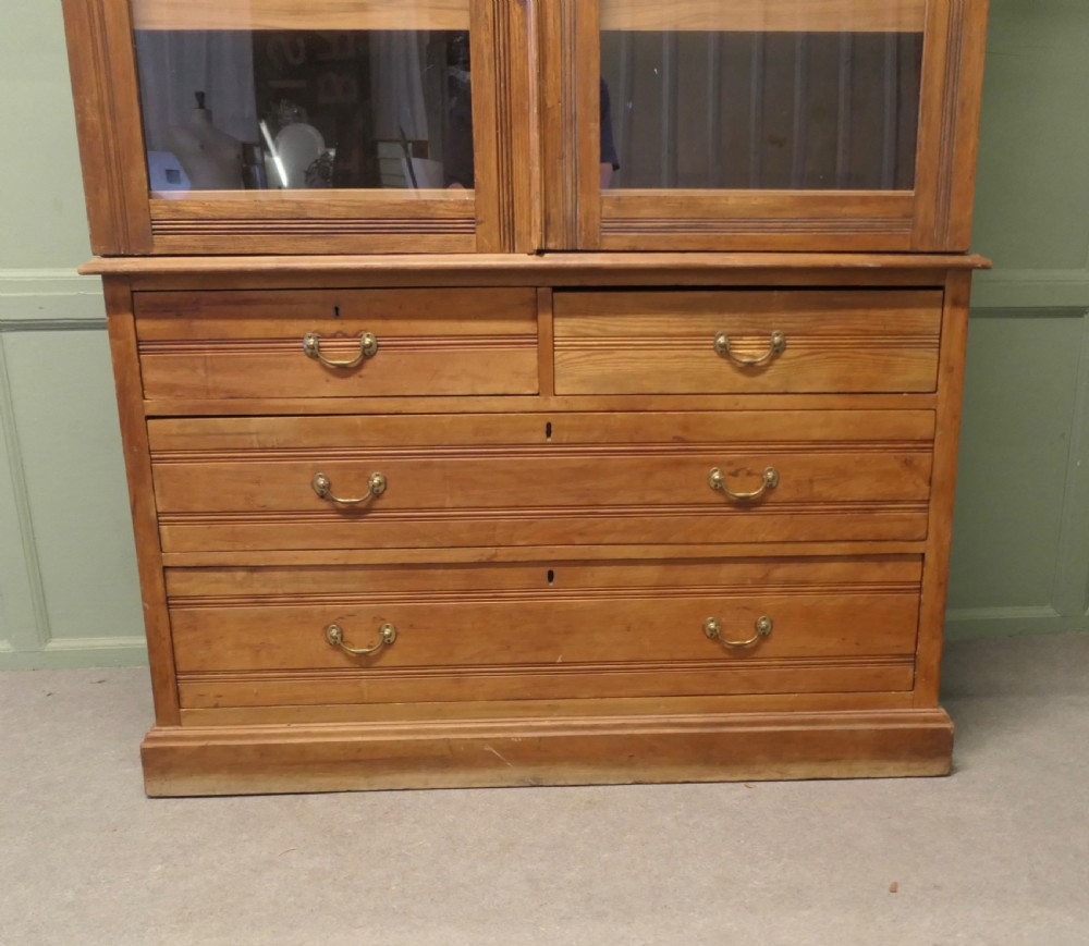 An Edwardian warm pine linen press with a glazed two-door upper cupboard revealing internal shelves above a base chest of four drawers. View III