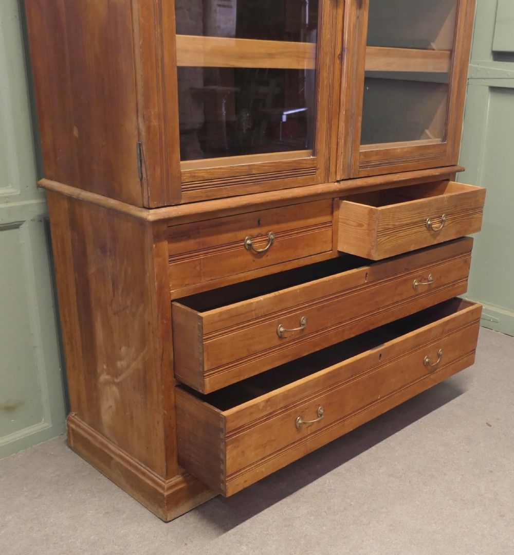 An Edwardian warm pine linen press with a glazed two-door upper cupboard revealing internal shelves above a base chest of four drawers. View V