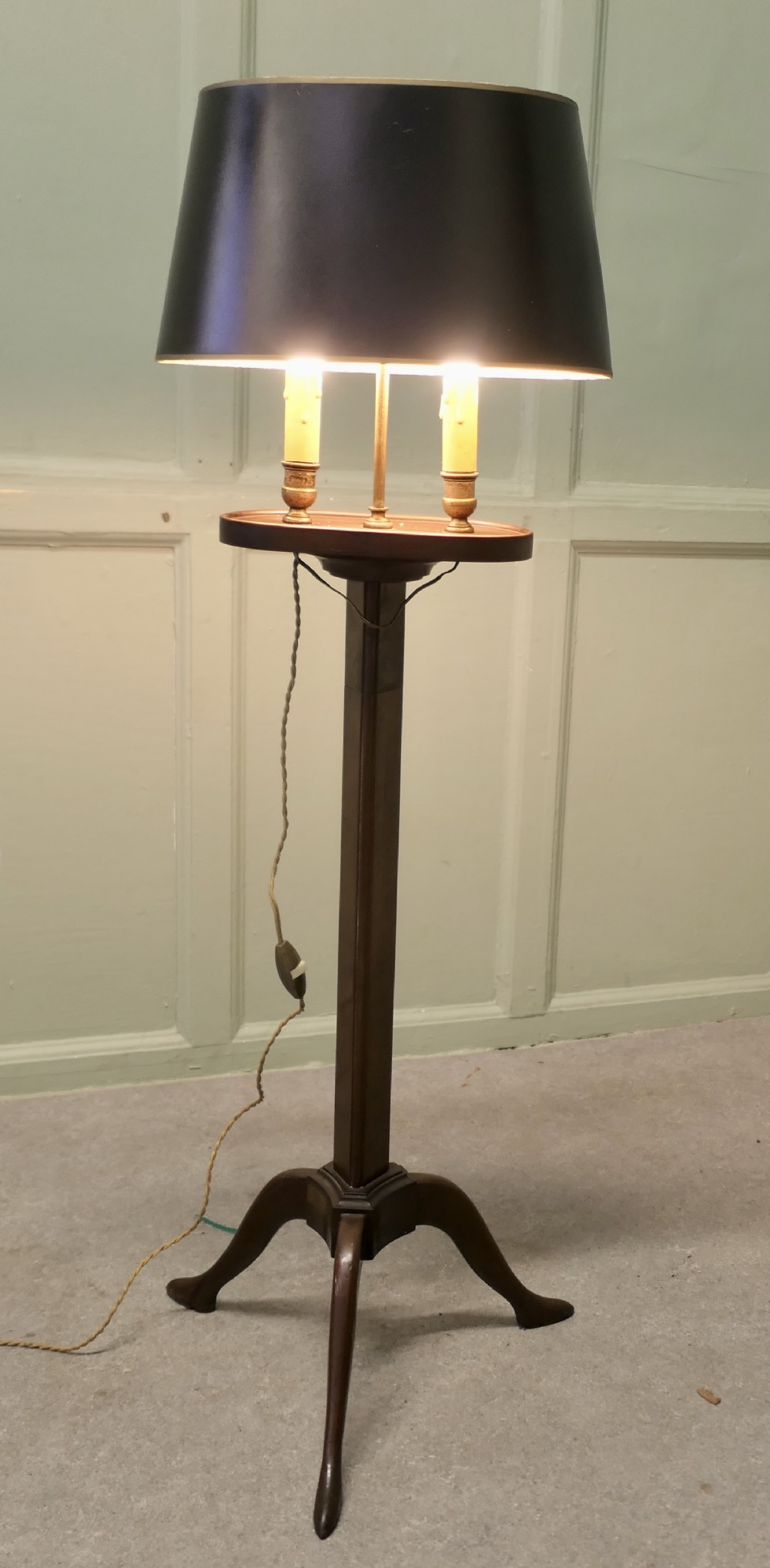 An antique mahogany bouillotte floor lamp featuring a dark oval shade mounted over twin faux-candle sockets on a tripod base.