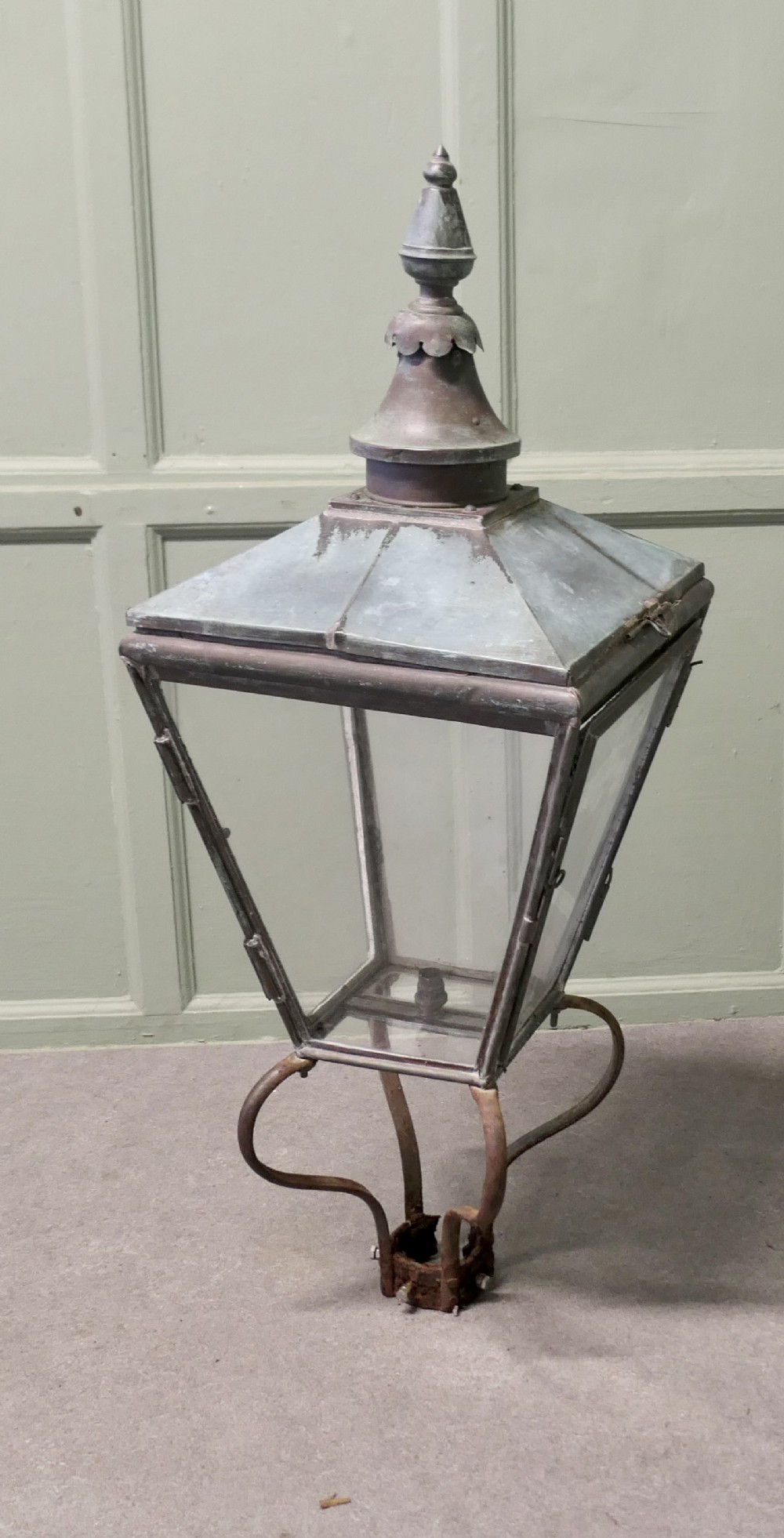 An antique Victorian copper street lantern featuring clear glass side panels, a tiered top capped with a finial, and a weathered verdigris patina.