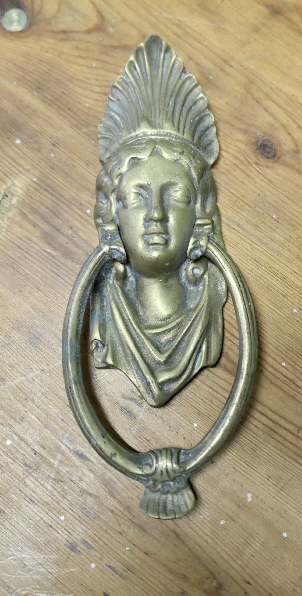 A cast brass Victorian door knocker featuring a classical female bust with a fan motif crown and an articulated oval ring.