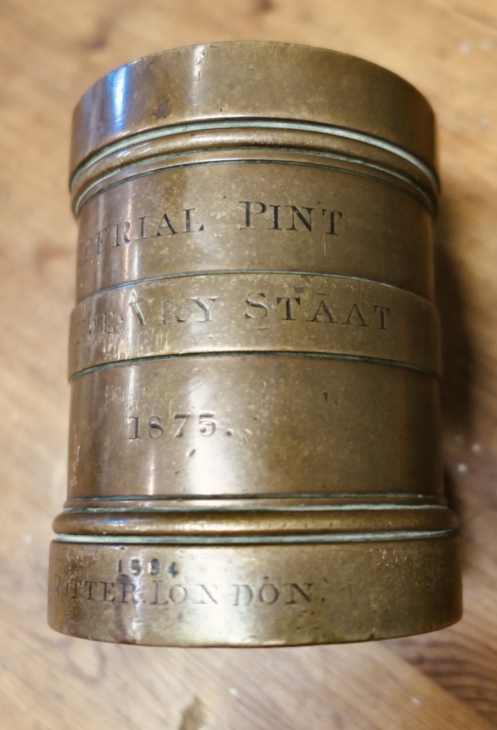 A cylindrical nineteenth-century cast bronze imperial pint measure with engraved lettering and official verification stamps.