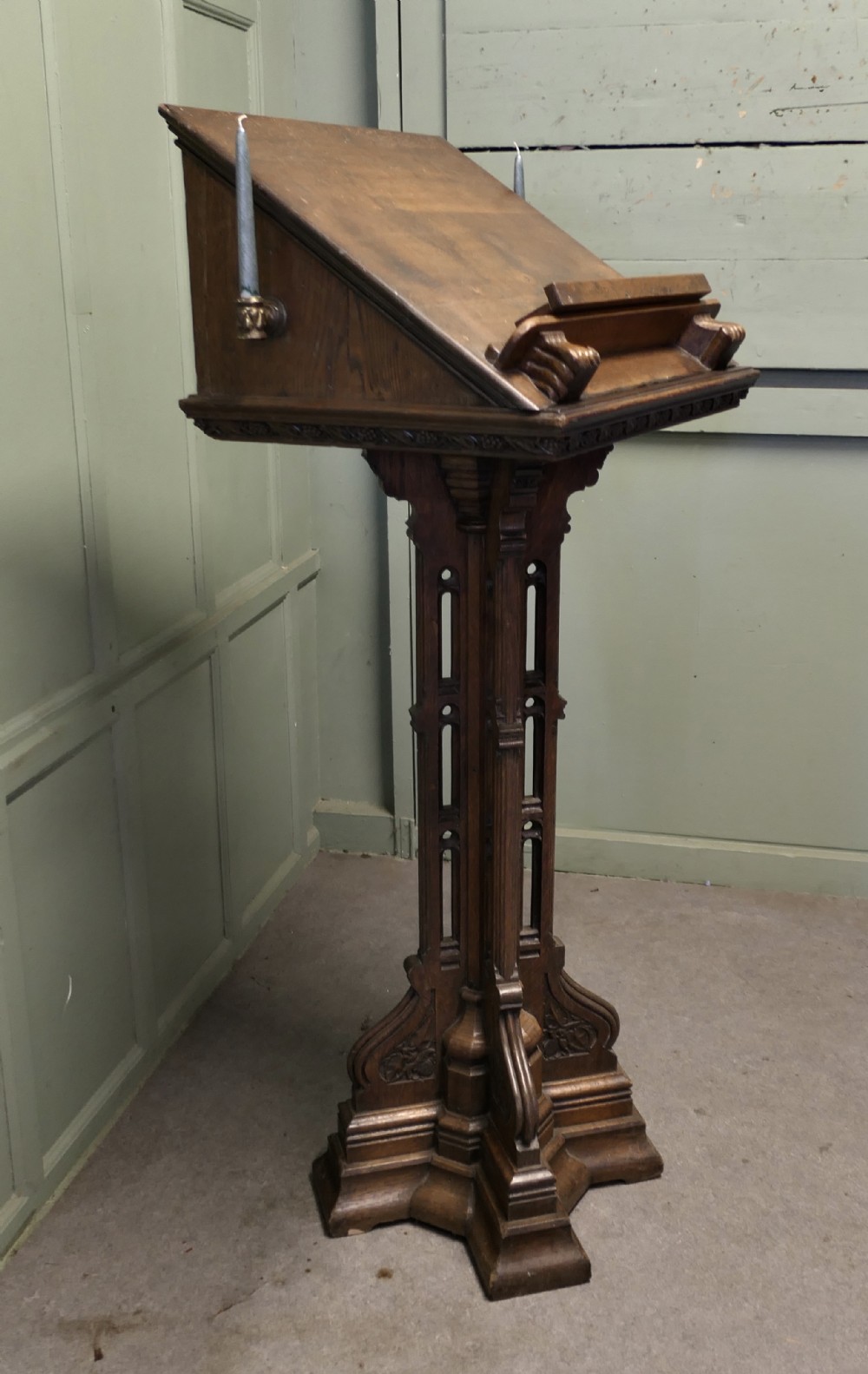 A 19th-century carved oak reading lectern featuring a sloped book rest, candle sconces, a traceried central column, and a stepped plinth base.