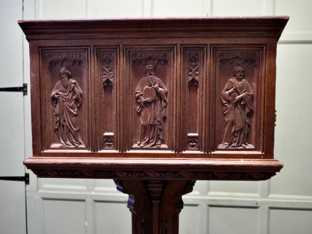 A 19th-century carved oak reading lectern featuring a sloped book rest, candle sconces, a traceried central column, and a stepped plinth base. View V
