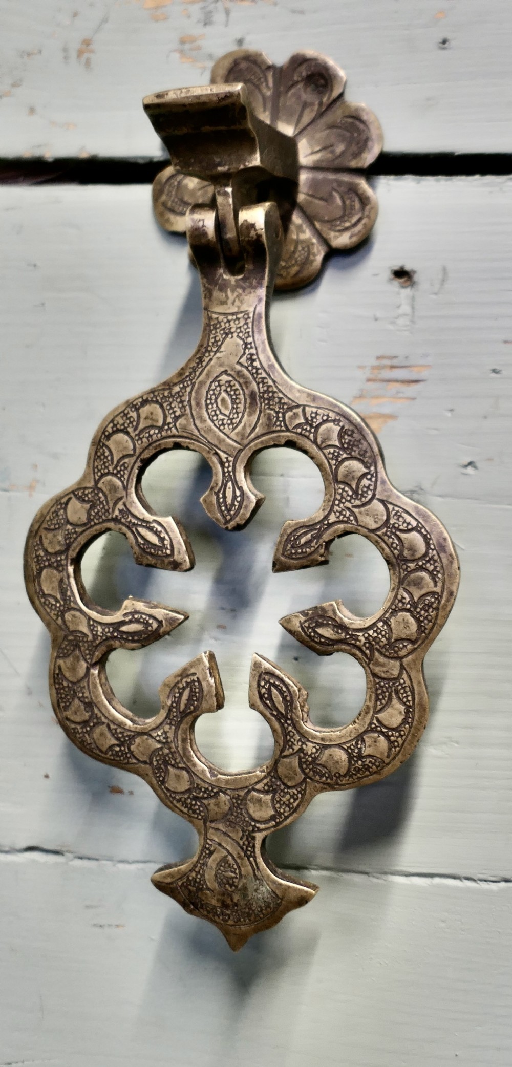 A large 19th-century pierced brass door knocker with intricate surface engraving and a flower-shaped mounting plate.