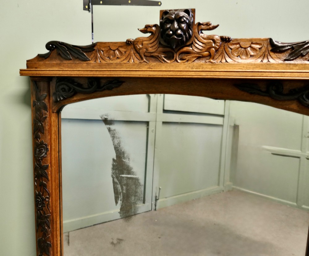 A large rectangular oak wall mirror featuring an arched glass top, relief foliate vine side carvings, and a crest with a carved lion mask. View III