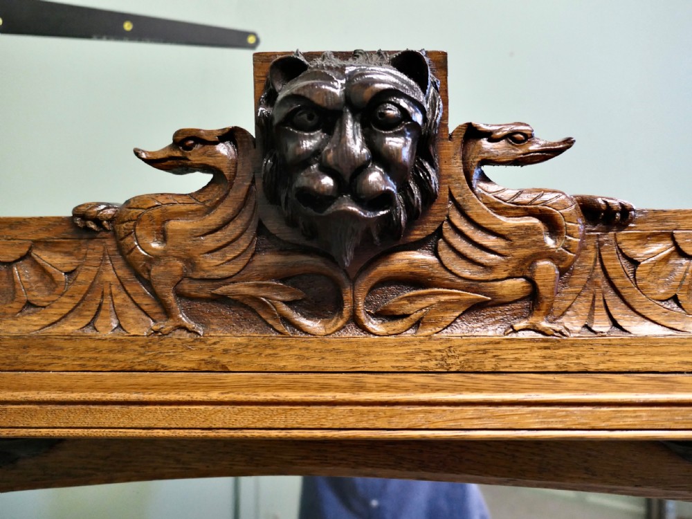 A large rectangular oak wall mirror featuring an arched glass top, relief foliate vine side carvings, and a crest with a carved lion mask. View V