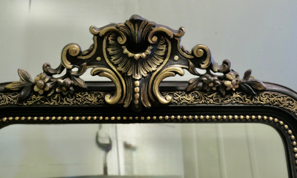 A tall rectangular ebonised pier mirror with rounded upper corners, an engraved gold leaf border, beaded moulding, and a carved central crest. View VI