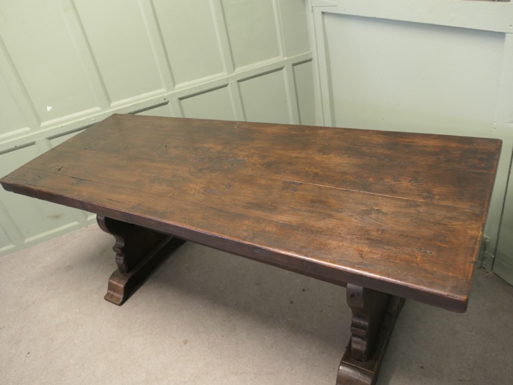 A solid dark oak French country refectory table featuring a thick rectangular top supported by twin trestle legs connected with a low central stretcher. View II