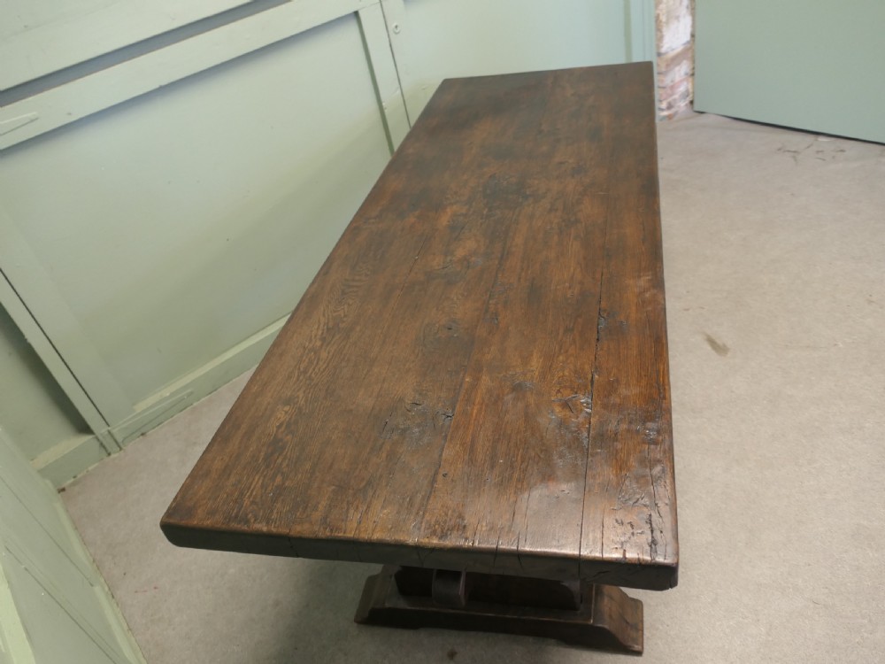 A solid dark oak French country refectory table featuring a thick rectangular top supported by twin trestle legs connected with a low central stretcher. View VI