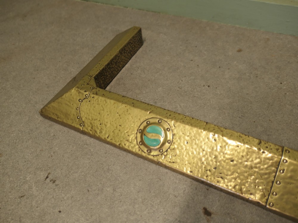 An antique Arts and Crafts brass fireplace fender featuring a hand-hammered texture, riveted joints, and circular green enamel cabochons. View II