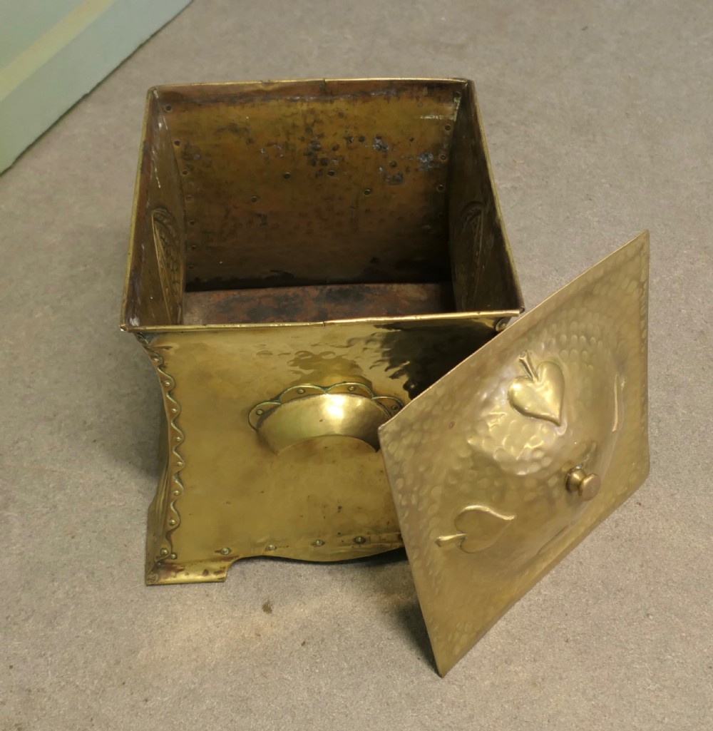 A hammered brass Arts and Crafts coal box featuring a domed lid and embossed spade-like floral motif on the front panel. View V