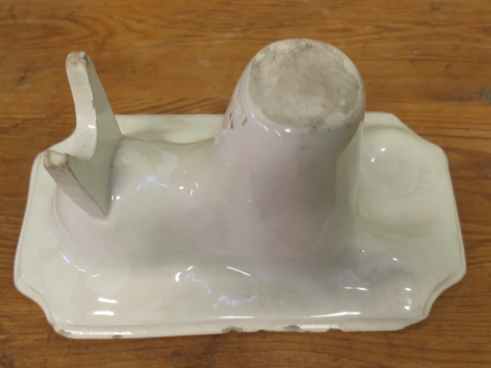 A cream glazed ceramic lion jelly mould viewed from the side showing its inverted rectangular base.