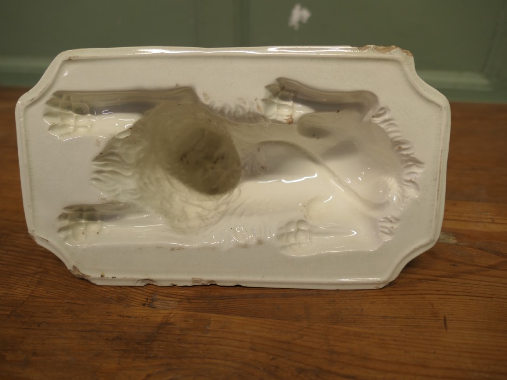 A cream glazed ceramic lion jelly mould viewed from the side showing its inverted rectangular base. View II