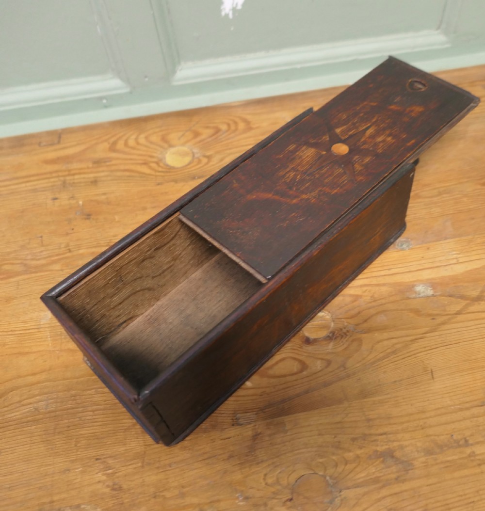 An 18th-century dark oak wall-hanging candle box featuring a shaped backboard and a sliding front panel carved with a star motif. View V