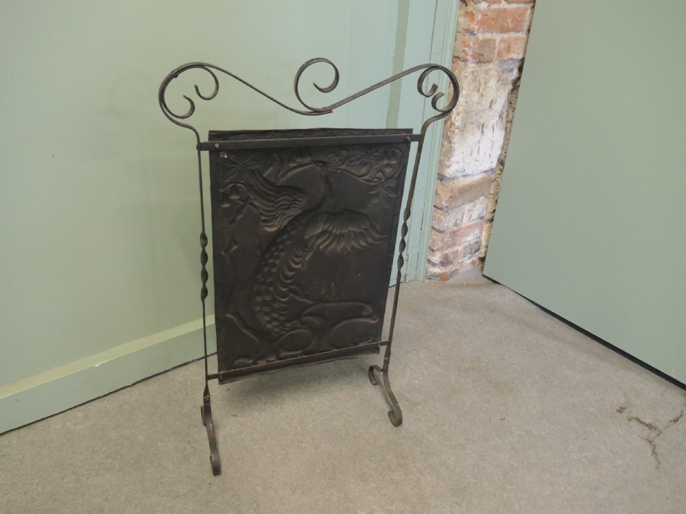 An Arts and Crafts wrought iron fire screen featuring a central embossed metal panel with a peacock motif framed by scrolled ironwork. View V