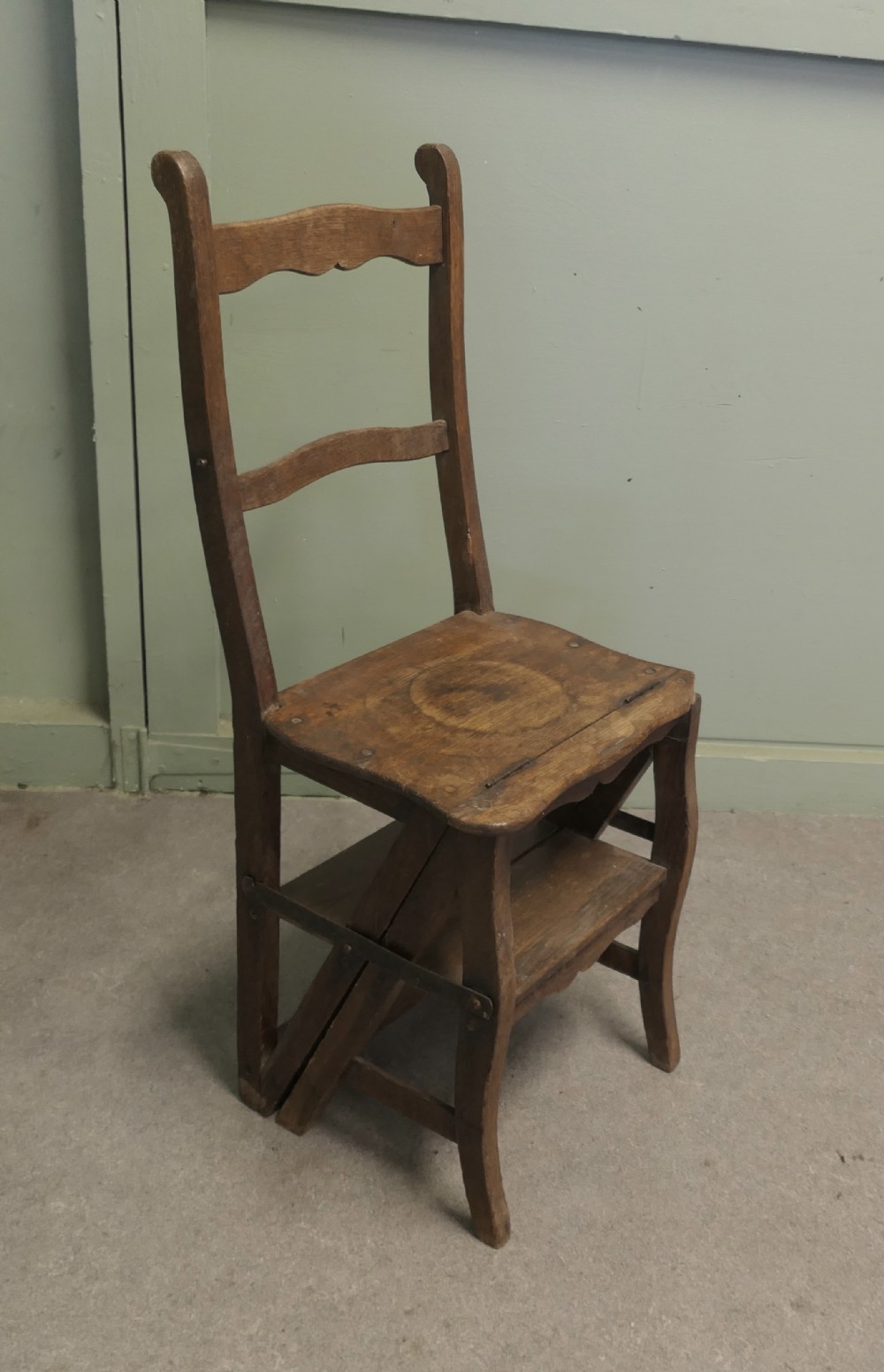 A rustic warm brown timber metamorphic chair with a carved ladder back that folds open into a set of small library steps.