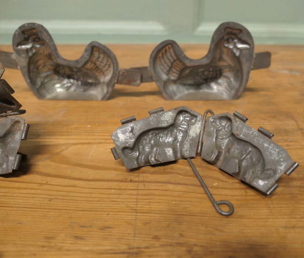 A set of four antique tinned metal chocolate moulds featuring shapes of a chicken, a dog, a cat, and a toque blanche chef hat. View VI