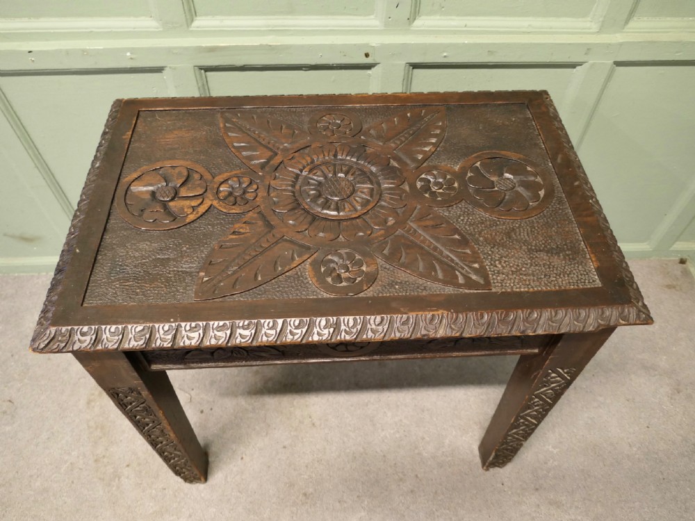 A dark oak side table featuring carved floral motifs on the top, carved apron borders, and four carved straight legs. View III