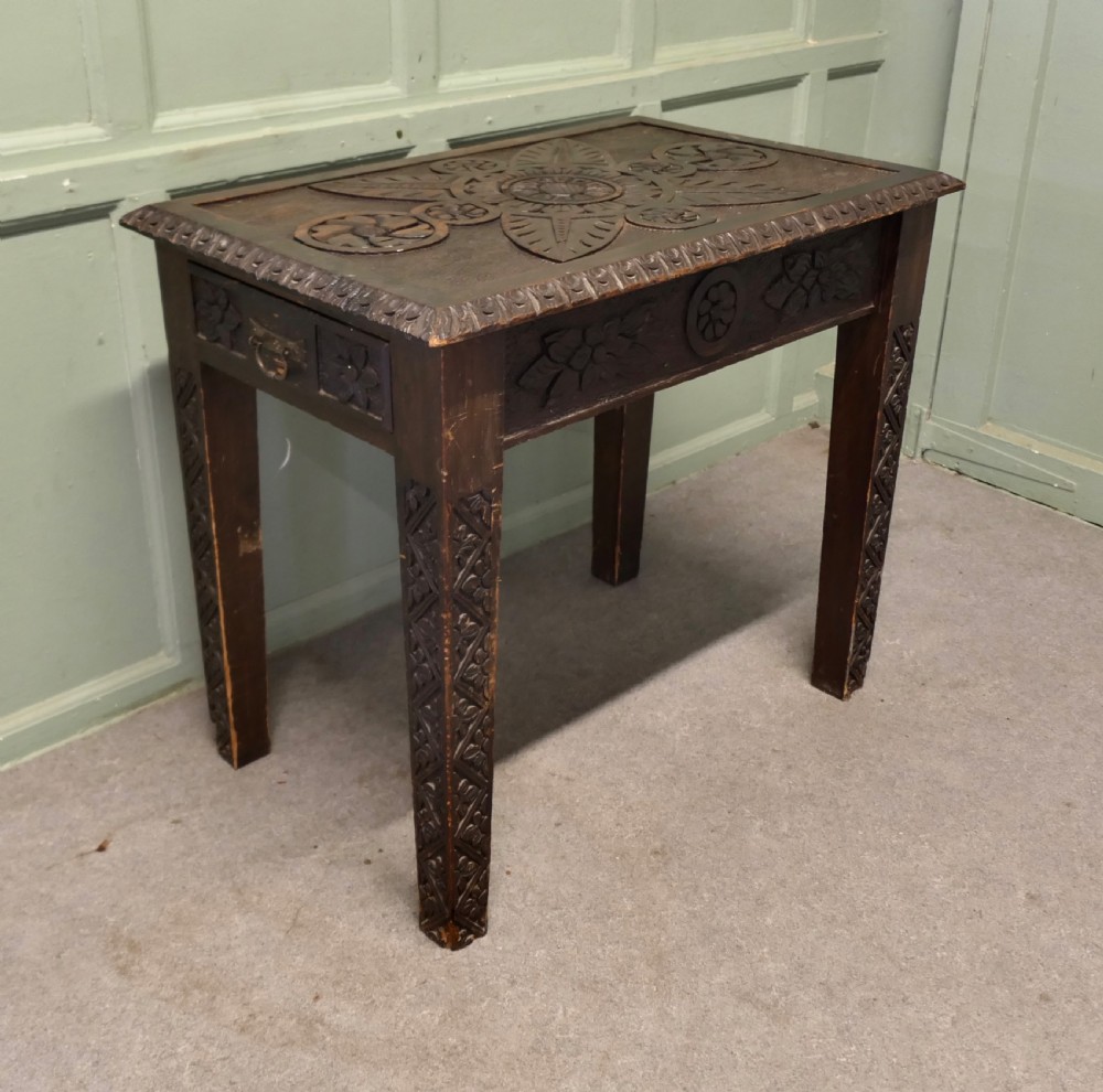 A dark oak side table featuring carved floral motifs on the top, carved apron borders, and four carved straight legs. View IV