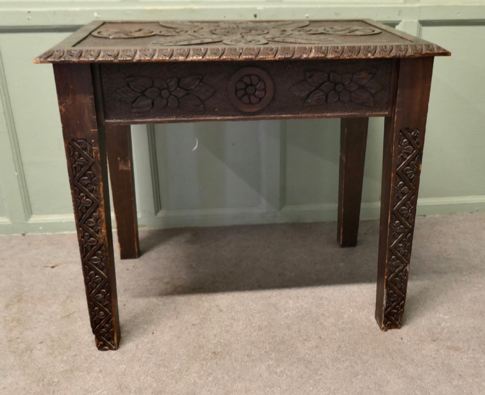 A dark oak side table featuring carved floral motifs on the top, carved apron borders, and four carved straight legs. View V