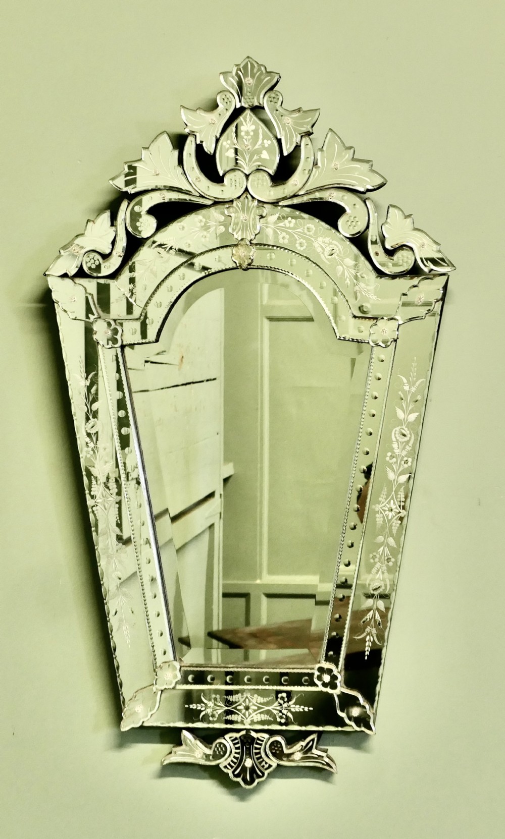A tall Art Deco Venetian wall mirror featuring hand-etched floral motifs, a contoured crest, and bevelled border panels.