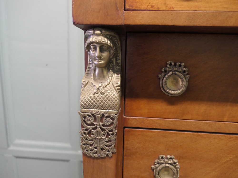 A tall French Empire style walnut chest of drawers featuring decorative metal mounts, caryatid corner figures, swan motifs, and claw feet. View V
