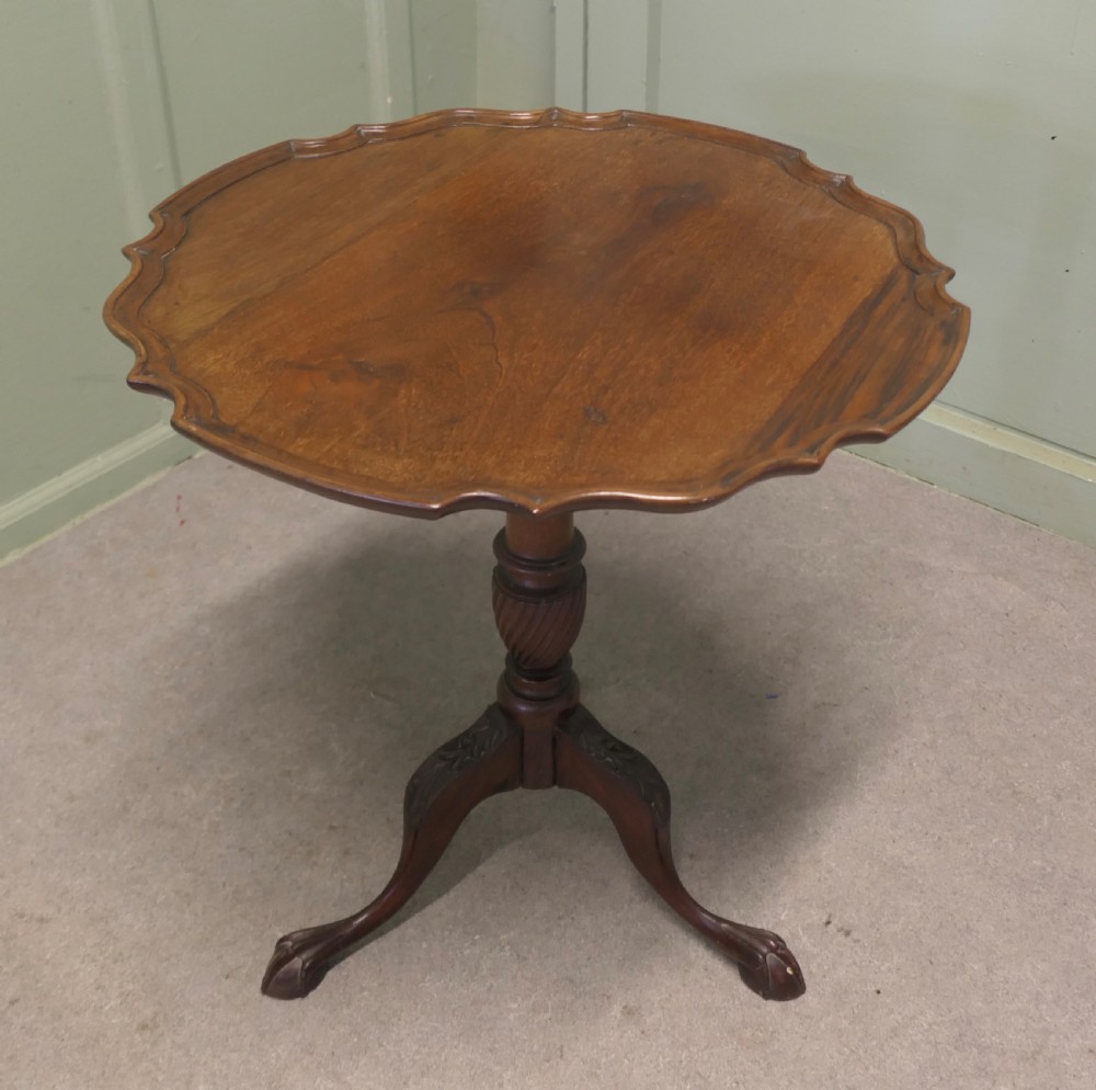 A 19th-century mahogany tilt-top wine table featuring a scalloped piecrust edge, turned central column, and carved tripod legs with claw feet.