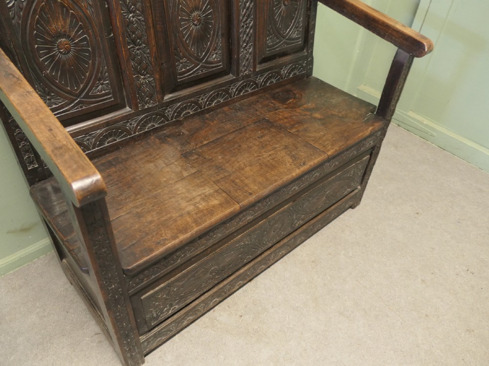 An eighteenth-century dark oak high back settle featuring intricately carved panels, straight armrests, and a lifted seat storage box. View V