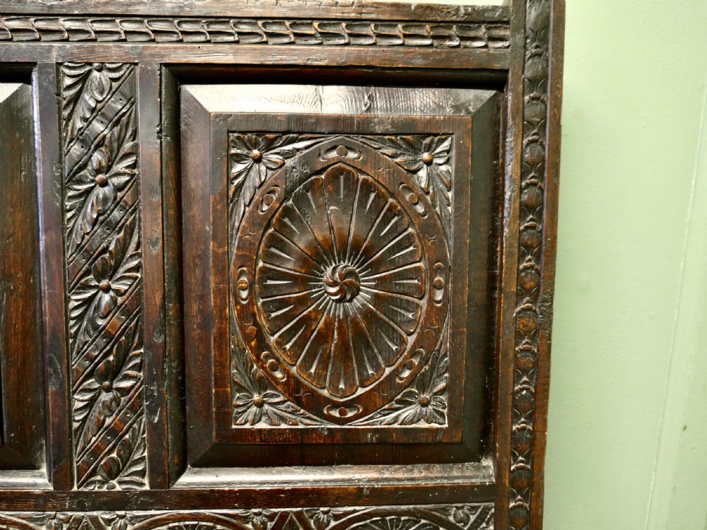 An eighteenth-century dark oak high back settle featuring intricately carved panels, straight armrests, and a lifted seat storage box. View VI