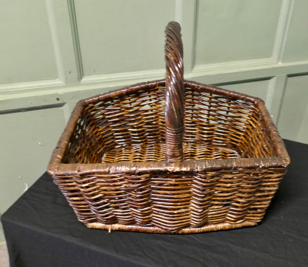 A dark brown woven wicker basket featuring a square base, flared sides, and a high twisted arched handle. View II