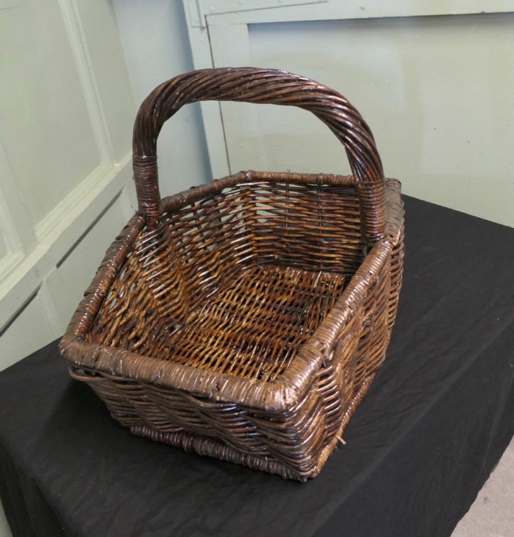 A dark brown woven wicker basket featuring a square base, flared sides, and a high twisted arched handle. View III