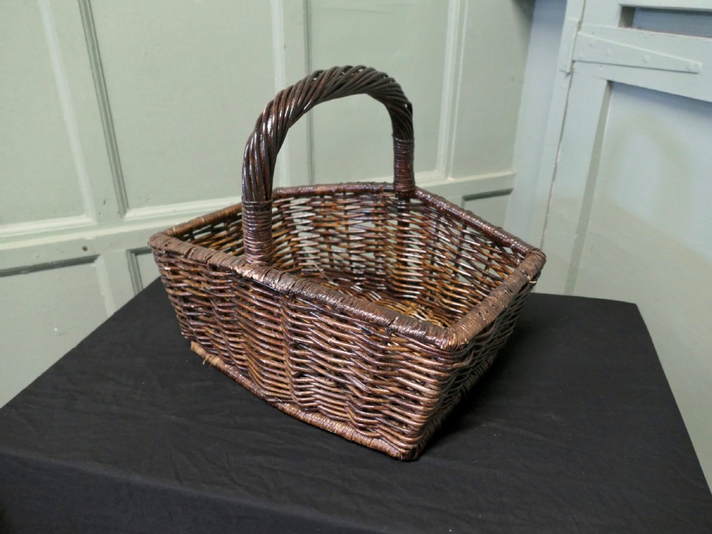 A dark brown woven wicker basket featuring a square base, flared sides, and a high twisted arched handle. View IV