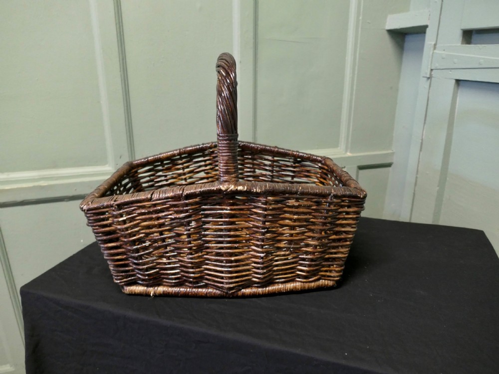 A dark brown woven wicker basket featuring a square base, flared sides, and a high twisted arched handle. View V