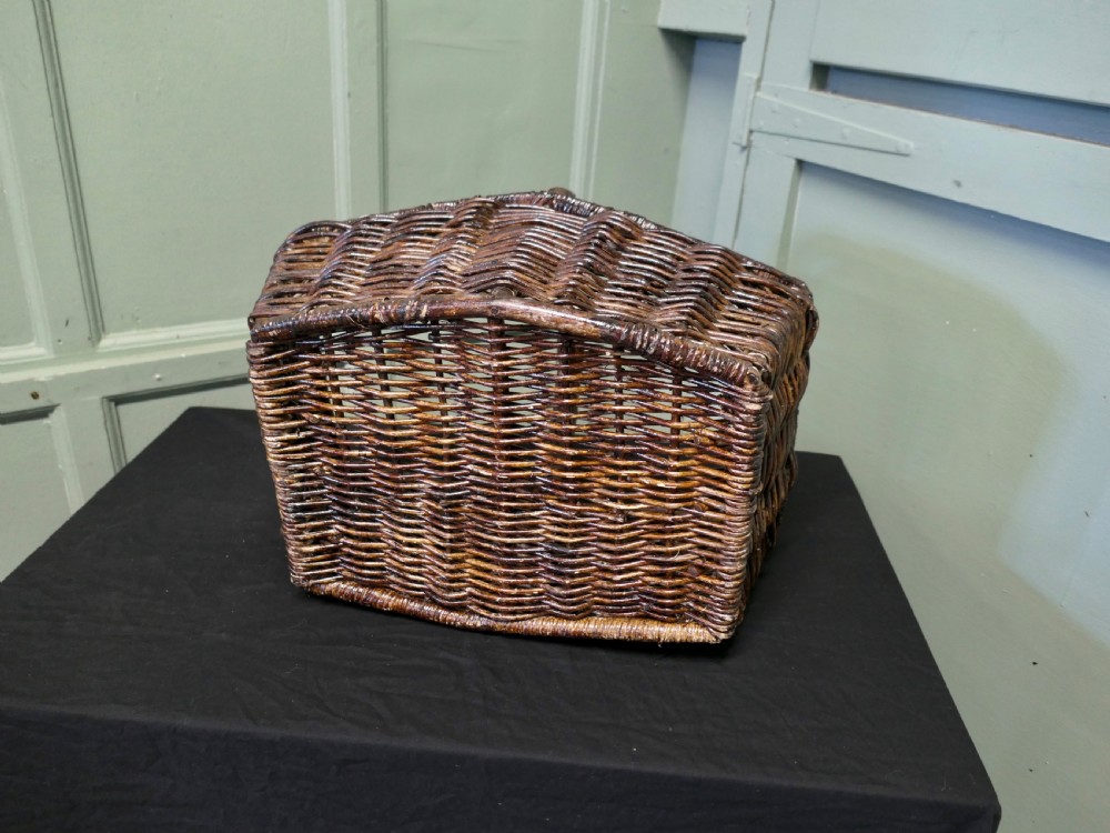 A dark brown woven wicker basket featuring a square base, flared sides, and a high twisted arched handle. View VI